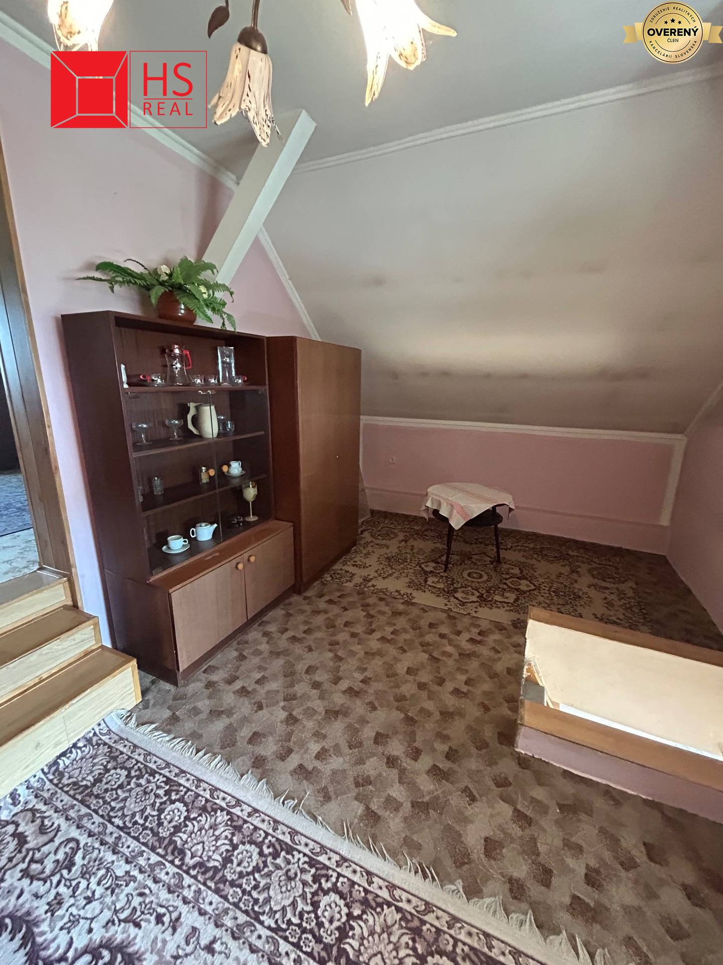Podkrovná miestnosť v rodinnom dome s kobercom, vitrínou a čalúneným stolčekom.
