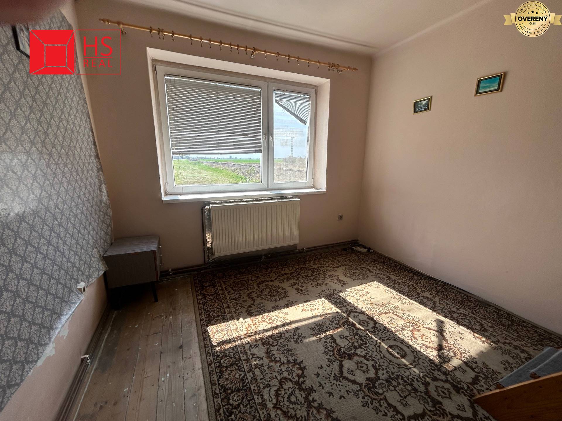 Izba v rodinnom dome s kobercom, oknom a radiátorom, podlaha s dreveným dekorom.