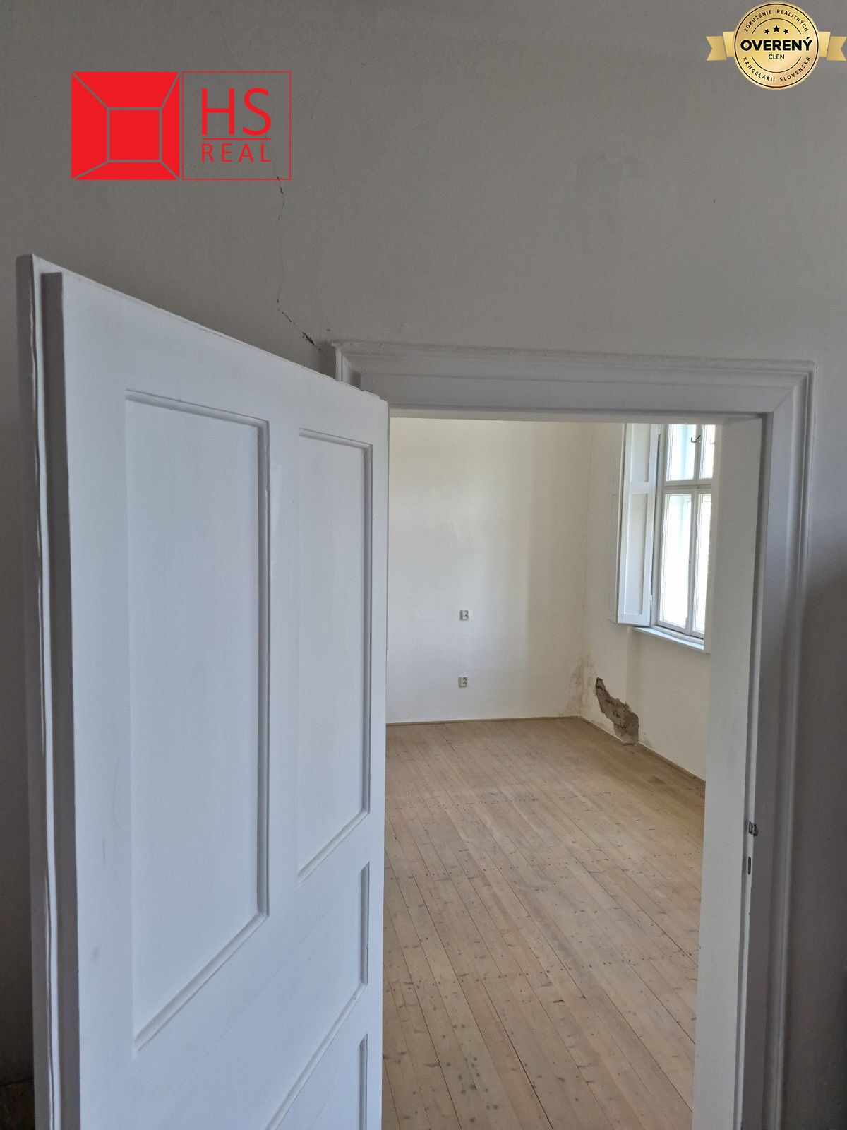 Biely interiér rodinného domu s poškodenou stenou, podlaha s dreveným dekorom.